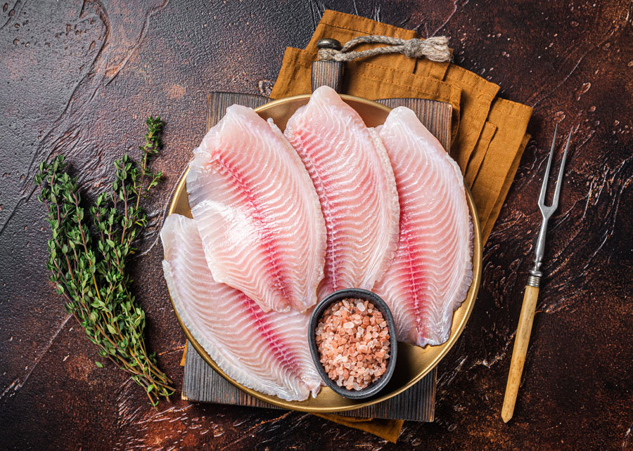 Raw fish fillet of tilapia in a plate with spices. Dark backgrou Raw fish fillet of tilapia in a plate with spices. Dark backgrou