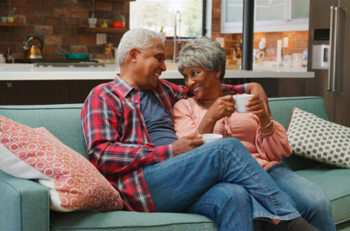 Smiling Senior Couple Relaxing With Hot Drink On Sofa At Home And Hugging