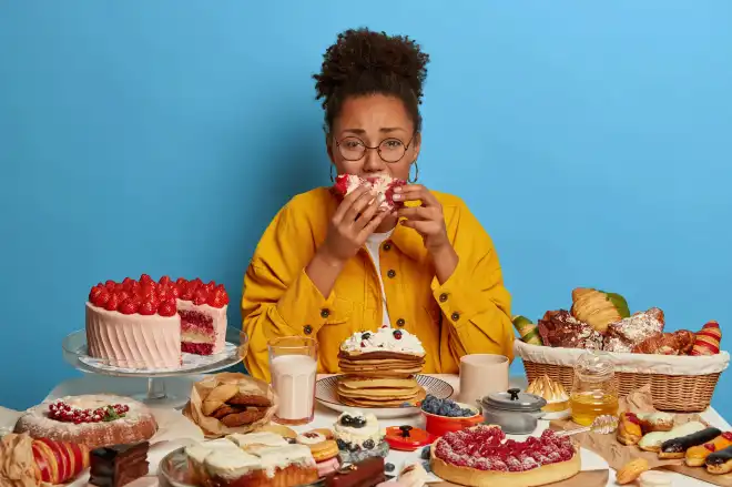 gluttony-overeating-concept-upset-crying-ethnic-woman-eats-piece-cake-reluctantly-sits-table-with-many-desserts-isolated-blue-wall gluttony-overeating-concept-upset-crying-ethnic-woman-eats-piece-cake-reluctantly-sits-table-with-many-desserts-isolated-blue-wall